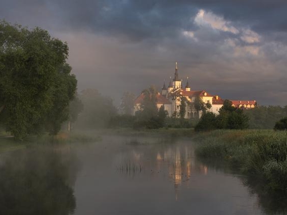 nad rzeką unosi się mgła, w oddali wyłaniają się zabudowania klasztorne i kościół
