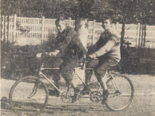 Skan czarno-białego zdjęcia z Gazety Białostockiej z 1972 roku. Na zdjęciu są dwaj młodzi mężczyźni siedzący na dwuosobowym rowerze-tandemie