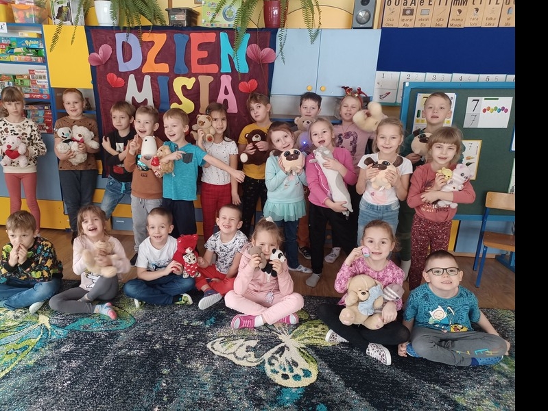 Duża grupa dzieci z misiami pozuje do zdjęcia w przdszkolnej sali