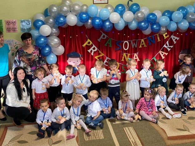 dzieci wraz z nauczycielami pozują do wspólnej fotografii na tle ściany udekorowanej w niebieskie balony