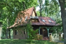 wśród zielonych drzew i trawy stoi maly drewniany budynek z brązowym dachem