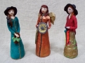 trzy gipsowe figurki kobiet w długich sukniach, dwie z nich mają na głowie kapelusze