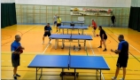 sala gimnastyczna, cztery stoły ustawione w rzędzie do gry w tenisa stołowego, przy każdym z nich po dwóch grających mężczyzn 