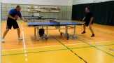 sala gimnastyczna, na pierwszym planie dwaj mężczyźni grający w tenisa stołowego 