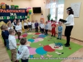 Na zdjęciu przedszkolaki stoja ustawione wokół krawędzi kolorowego dywanu. Po prawej stronie stoi pani dyrektor, w ręku trzyma książkę.