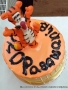 Na zdjęciu pomarańczowy tort z napisem: Pasowanie. Na torcie znajduje się figurka tygryska z bajki "Kubuś Puchatek".