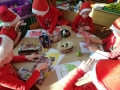 Na zdjęciu dzieci siedzą przy stoliku i rysują kredkami na kartkach worki świętego Mikołaja. Na stolikach leżą równiez piórniki na kredki. Dzieci ozdabiają rysunki wycinankami z gazetek.