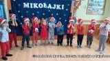 Dzieci stoją w rzędzie, za nimi na ścianie na niebieskim tle biały napis Mikołajki.