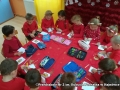 Dzieci siedzą przy stoliku nakrytym czerwonym obrusem. Na stoliku leżą piórniki, dzieci wykonuja pracę plastyczną.