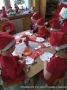 Zdjęcie przedstawia dzieci siedzące przy stoliku i wykonujące m.in. z papierowych talerzyków postać świętego Mikołaja.