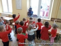 Dzieci stoją przed oknem i machają do świętego Mikołaja, który stoi za szybą.
