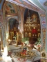 wnętrze świątynii ukazane z góry; stoi anałoj z ikoną, po obu stronach obok niego stoją świeczniki; na wprost widoczny jest drewniany ikonostas w ikonami; na ścianach widnieją polichronie z wizerunkami świętych
