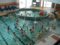 ludzie kąpiacy sie w jednym z basenów; na wprost umieszczony jest mniejszy basen w kształcie koła, w którym pływa duża pomarańczowa piłka