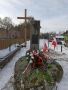 Na zdjęciu widać trzy krzyże, polskie flagi oraz pomnik, na którym leżą biało – czerwone kwiaty.