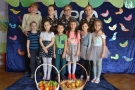 Na zdjęciu dzieci i panie stoją za koszami z owocami.