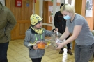 Na zdjęciu chłopiec wrzuca pieniądze do przezroczystej skrzynki, którą trzyma jedna z organizatorek kiermaszu. W drugiej ręce chłopiec trzyma wybraną przez siebie ozdobę: pomarańczowy koszyczek.