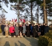 Zdjęcie grupowe samorządowców, duchownych i władz mundutowych, za nimi wysoki metalowy krzyż