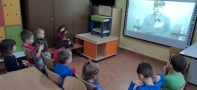 Przedszkolaki siedzą na krzesełkach i oglądają film o Marszałku Piłsudskim.