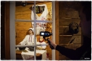 Z prawej strony stoi osoba trzymająca kamerę nakierowana na wystawę manekinów w scenerii białoruskiej chaty.