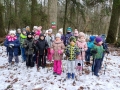 Dzieci stoją w grupie przy drzewie, na którym widać oznaczenie dla trasy nordic walking. 