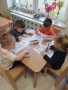 Czworo dzieci siedzi przy stoliku i kolorują kolorowanki.