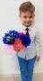 Chłopiec w eleganckiej koszuli trzyma kwiaty z bibuły.