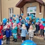 Dzieci stoją przed budynkiem, trzymają niebieskie balony.