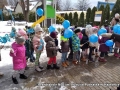 Dzieci stoją na chodniku, wokół leży śnieg.