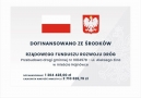 tablica informacyjna projektu; u góry obok siebie flaga i godło Polski, niżej nazwa inwestycji i koszt calkowity oraz kwota dofinansowania