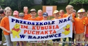 Dzieci w pomarańczowych koszulkach trzymają transparent z nazwa przedszkola, do którego uczęszczają