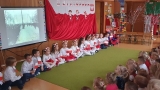 Dzieci siedzą na dywanie, trzymając biało - czerwone flagi.