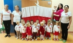Zdjęcie grupowe dzieci i opiekunek,  w tle biało - czerwona flaga.
