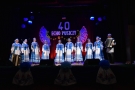 Na scenie stoją członkowie zespołu ubrani w biało-błękitne stroje.