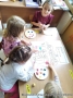 Dzieci siedzą przy stole i malują farbami rysunek przedstawiający dzieci.