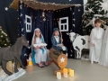 Zdjęcie przedstawia scenę z Jasełek w wykonaniu dzieci, prezentującą Marię i Józefa siedzących z szopie betlejemskiej.