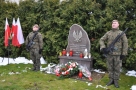 żołnierze przy pomniku stoją na warcie. Z lewej strony widać trzy polskie flagi.