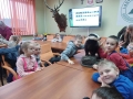 Dzieci siedzą przy stole, oglądają eksponaty leśnych zwierząt.