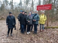Grupy osób stoi w lesie przy znaku Rezerwat Krajobrazowy Władysława Szafera 