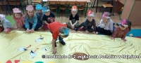 Dzieci siedzą na dywanie. Jedno dziecko pokazuje rysunek bociana