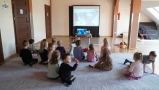 Dzieci siedzą na dywanie i oglądają film.