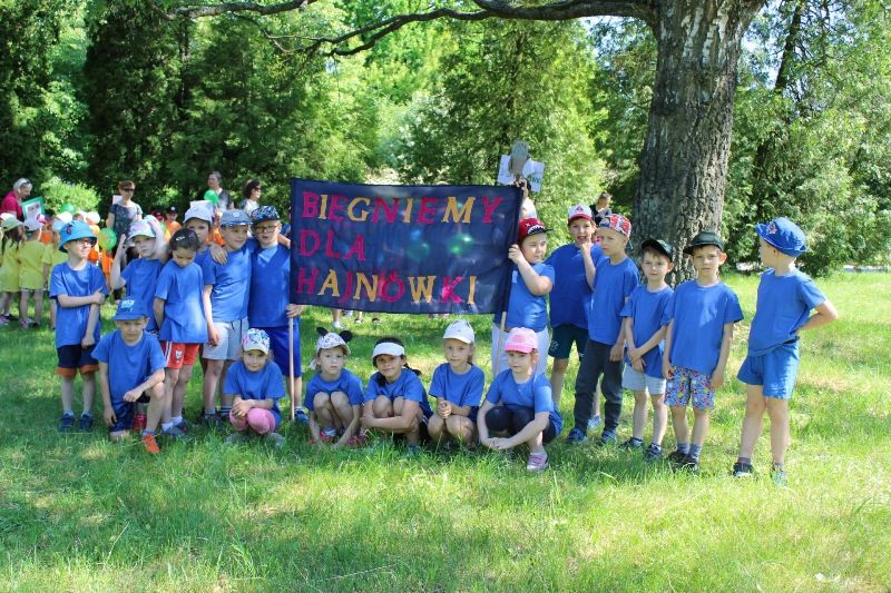 Przedszkolaki ubrane w jednakowe niebieskie koszulki trzymają plakat z napisem "Biegniemy dla Hajnówki"