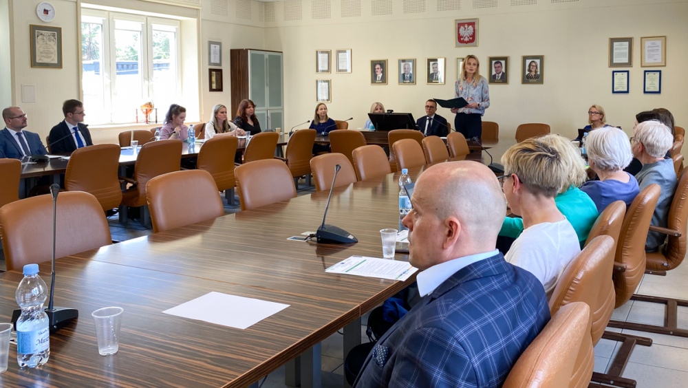 Kilkanaście osób siedzi przy stole konferencyjnym