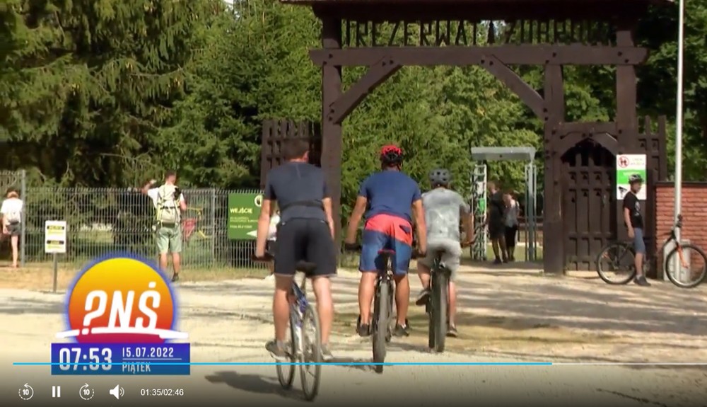 rowerzyście jadą w stronę  dużej drewnianej bramy "Rezerwatu żubrów"