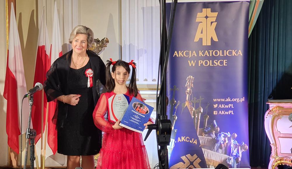 dziewczynka z dyplomem stoi obok kobiety w sali Zamku Królewskiego