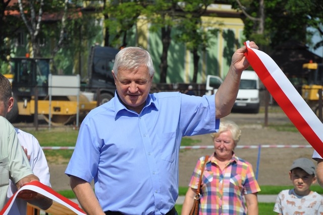 Burmistrz Miasta unosi w lewej dłoni przecięta biało - czerwona wstęgę.