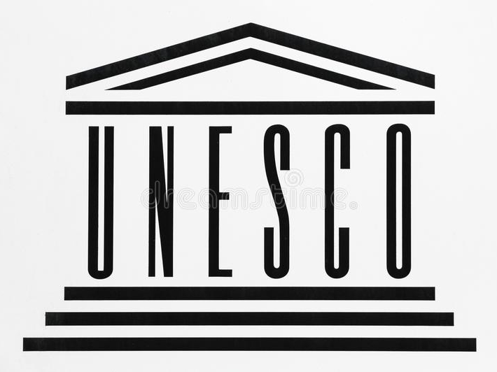 Logo przedstawia napis wielkimi literami: UNESCO. pod napisem znajdują się trzy poziome linie, a nad nim trójkąt w kształcie dachu.