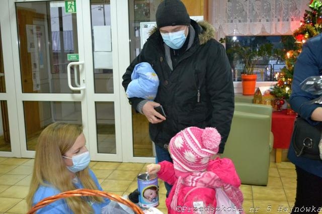 Na zdjęciu Dziecko w óżowej czapce i kurtce wrzuca pieniążek do puszki.