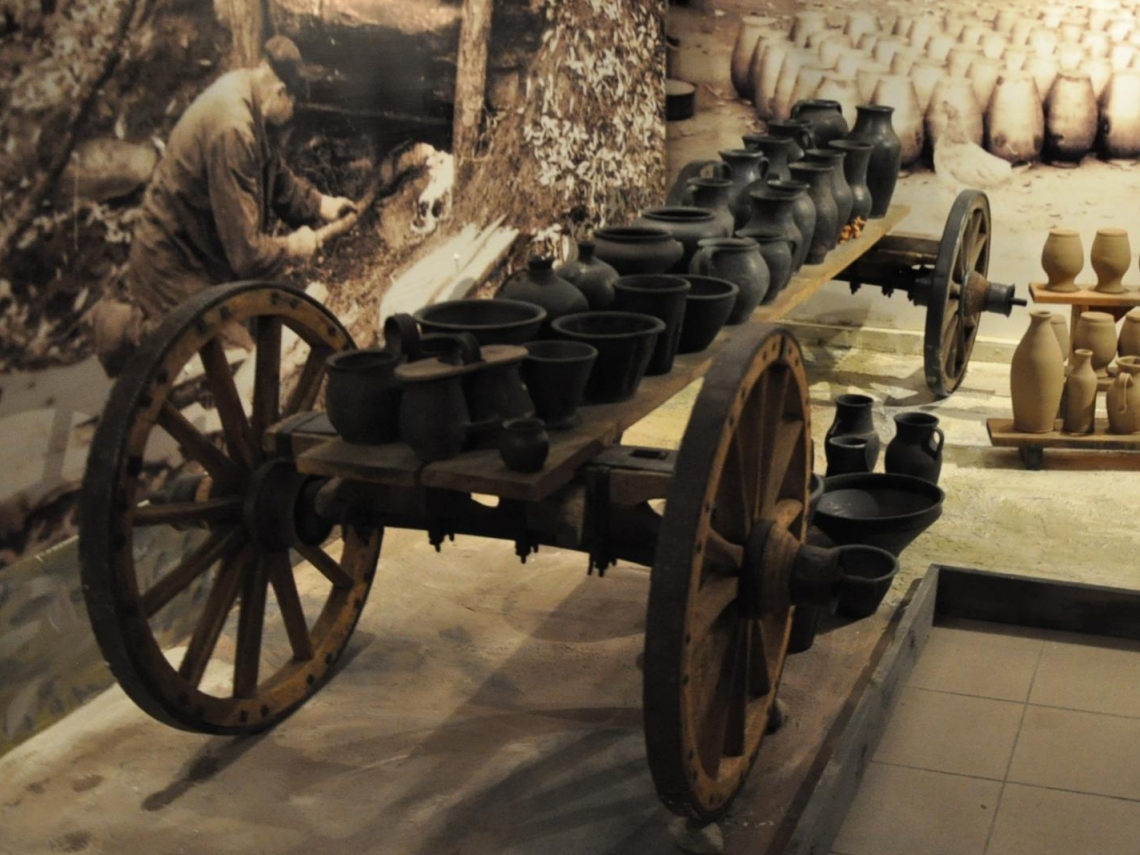 Element jednej z ekspozycji wystawowej: drewniany wóz na którym stoją gliniane naczynia, przed nim mniejsze narzędzia używane w gospodarstwach domowych na wsiach 