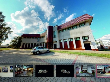 Na zdjęciu znajduje się budynek muzeum, otoczony parkingami oraz zielenią