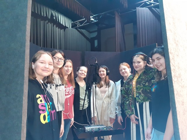 Osiem dziewcząt stoi przy sprzęcie nagrywającym.